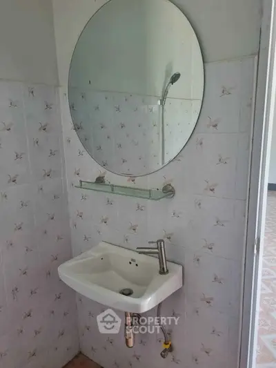 Compact bathroom with round mirror and wall-mounted sink, featuring floral tile design.