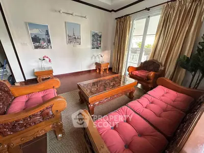 Elegant living room with wooden furniture and large windows opening to a balcony, perfect for relaxation.