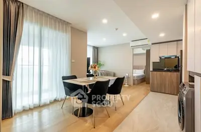 Modern open-plan living room with dining area and kitchen, featuring sleek furniture and natural light.