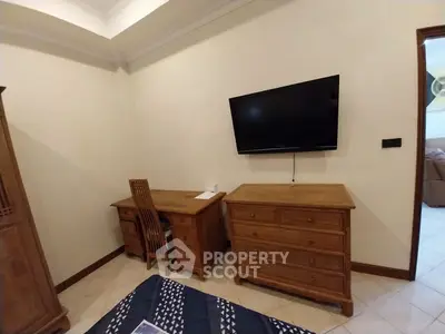 Cozy bedroom with wooden furniture and wall-mounted TV, perfect for relaxation and work-from-home setup.