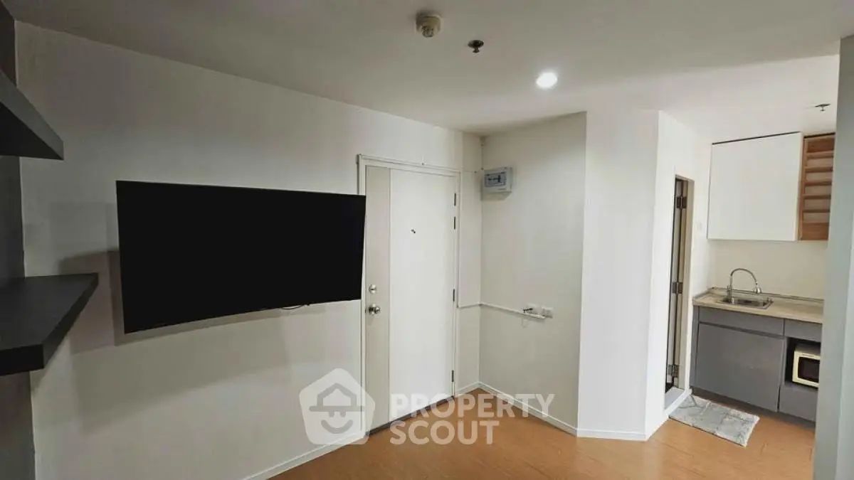 Modern apartment interior with wall-mounted TV and compact kitchen area.
