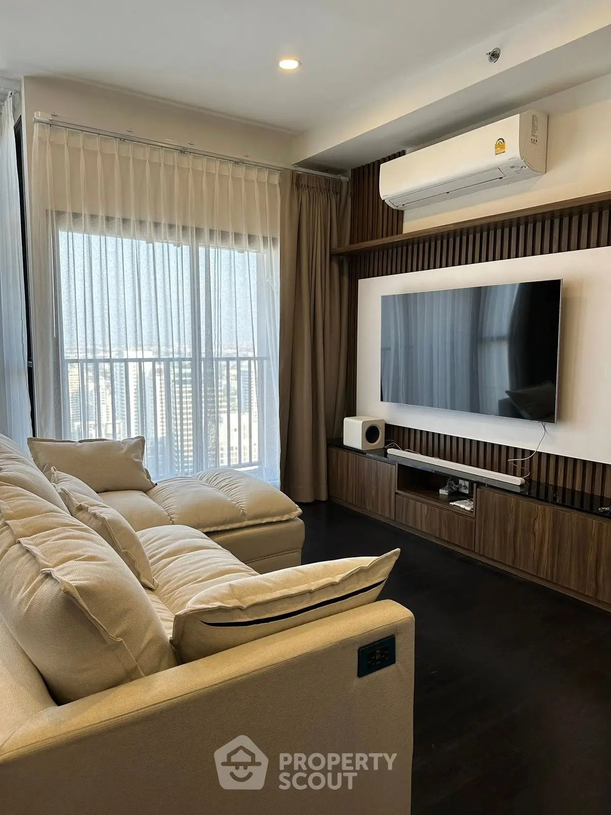 Modern living room with large TV, cozy sofa, and city view through sheer curtains.