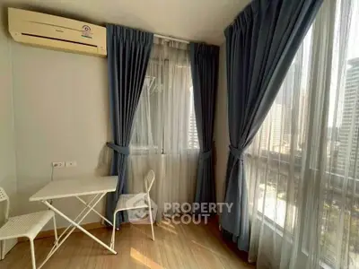 Bright corner unit with large windows and city view, featuring a cozy seating area and elegant curtains.
