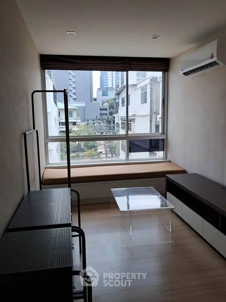 Modern living room with large window and city view, featuring minimalist furniture and air conditioning.