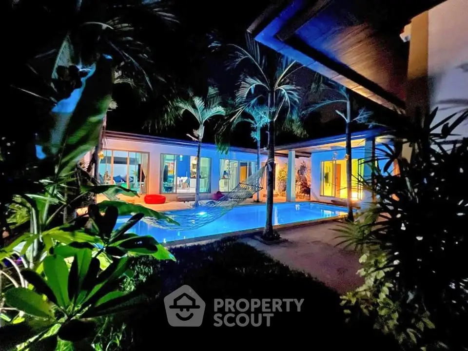 Luxurious tropical villa with illuminated pool and lush garden at night, perfect for serene living.