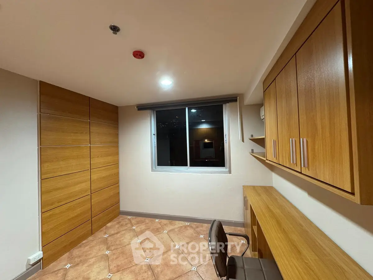 Modern study room with wooden cabinets and desk, featuring a large window for natural light.
