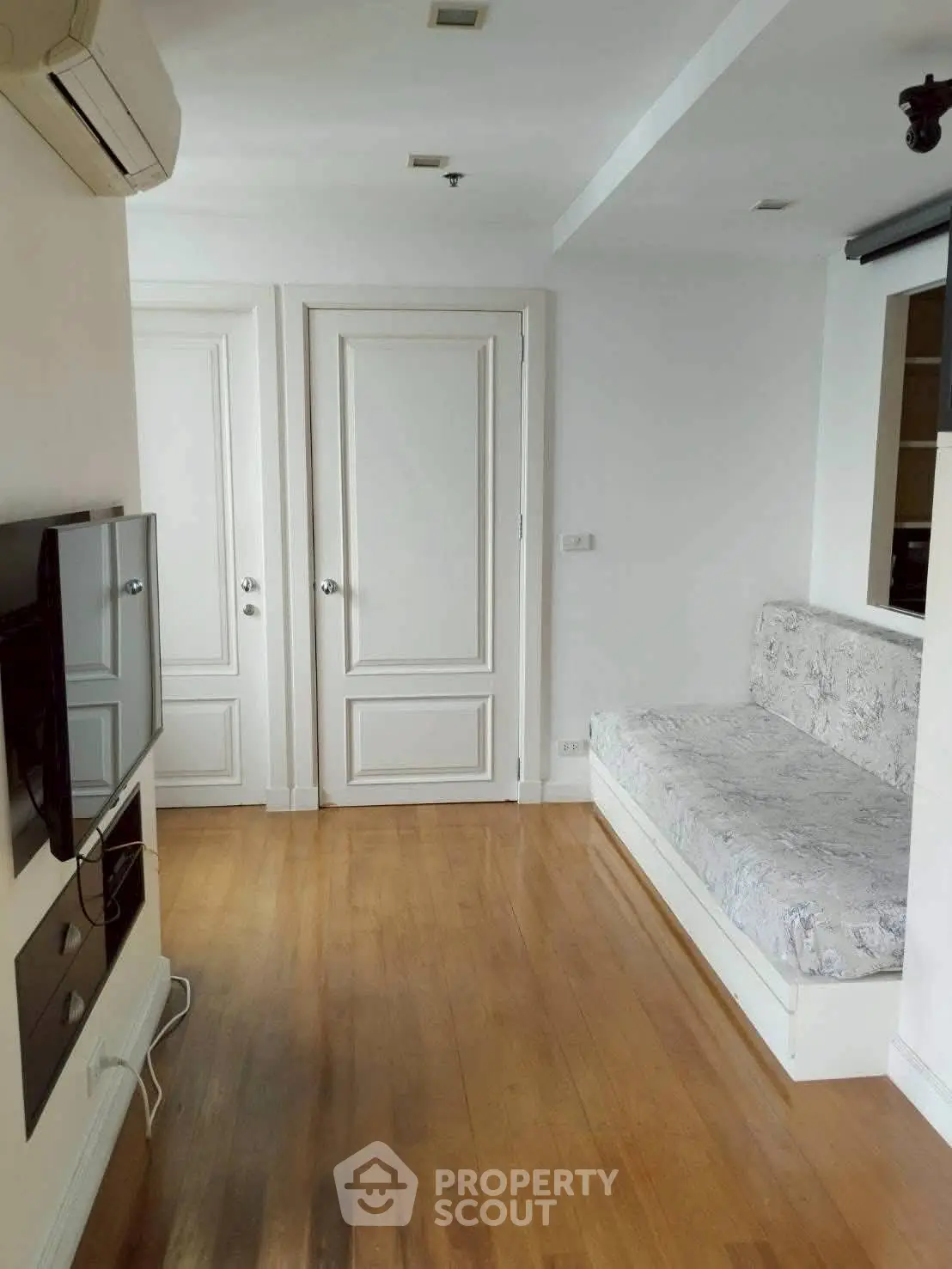 Spacious living room with wooden flooring and wall-mounted TV, featuring a cozy built-in sofa.