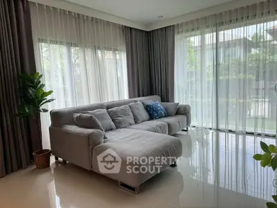 Spacious living room with modern gray sectional sofa and large windows offering lush garden views.