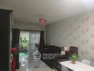 Charming living room with floral wallpaper and cozy seating area, leading to a lush balcony view.