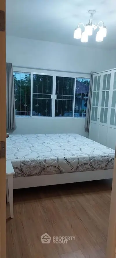 Cozy bedroom with large windows and wooden flooring, perfect for relaxation.