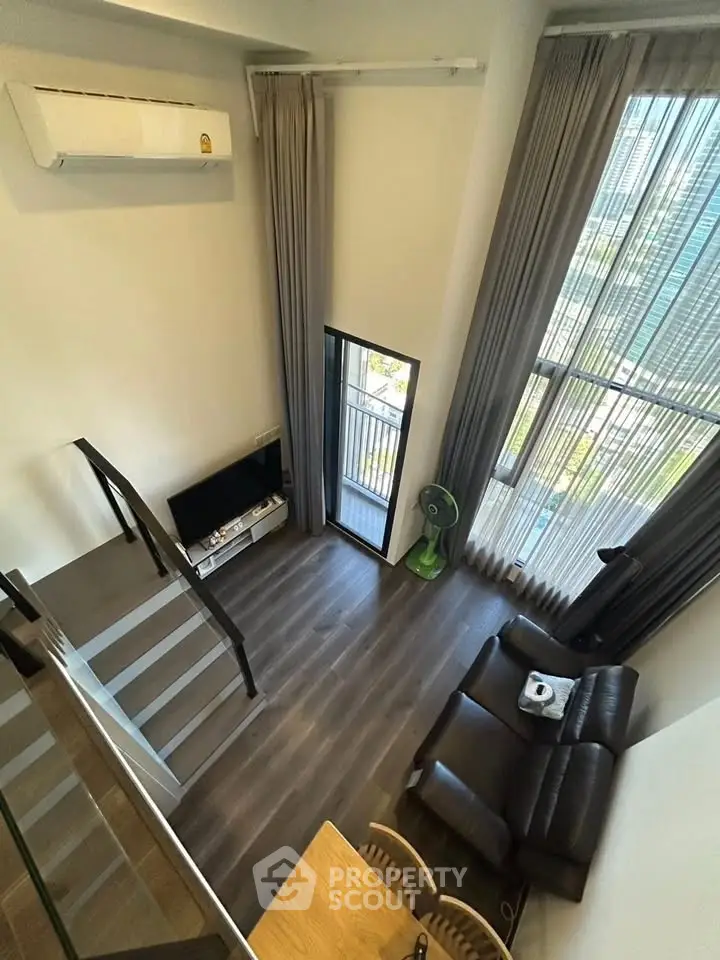 Modern loft apartment with high ceilings and large windows offering a stunning view, featuring a cozy living area.