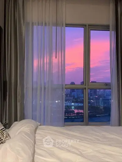 Stunning bedroom view with vibrant sunset over city skyline, perfect for urban living enthusiasts.