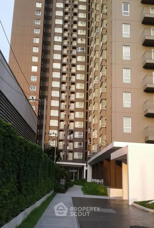 Modern high-rise apartment building with lush greenery and paved walkway entrance.