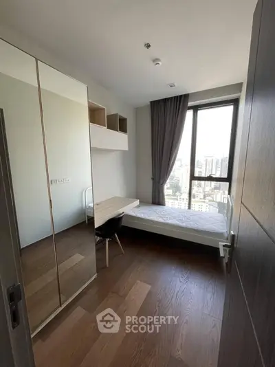 Modern bedroom with city view, featuring sleek furniture and large window for natural light.