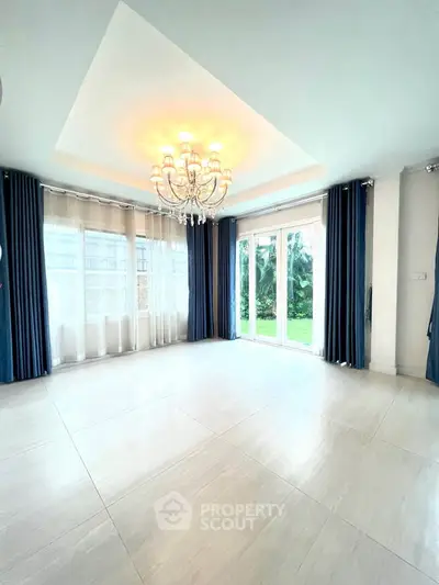 Spacious living room with elegant chandelier and large windows overlooking garden