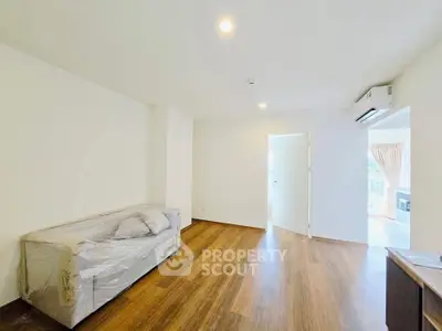 Spacious living room with wooden flooring and natural light, featuring a covered sofa and air conditioning.