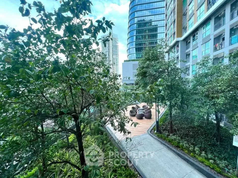 Modern urban garden with lush greenery and seating area in a high-rise residential complex.