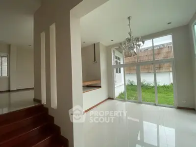 Spacious modern living room with large windows and garden view, featuring elegant chandelier and open layout.