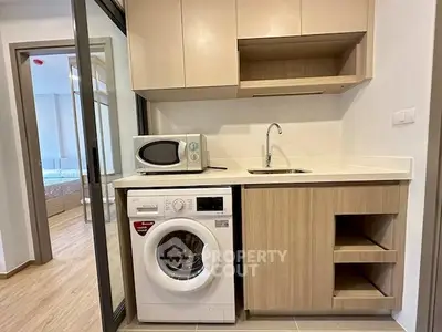 Modern compact kitchen with washing machine and microwave in stylish apartment.