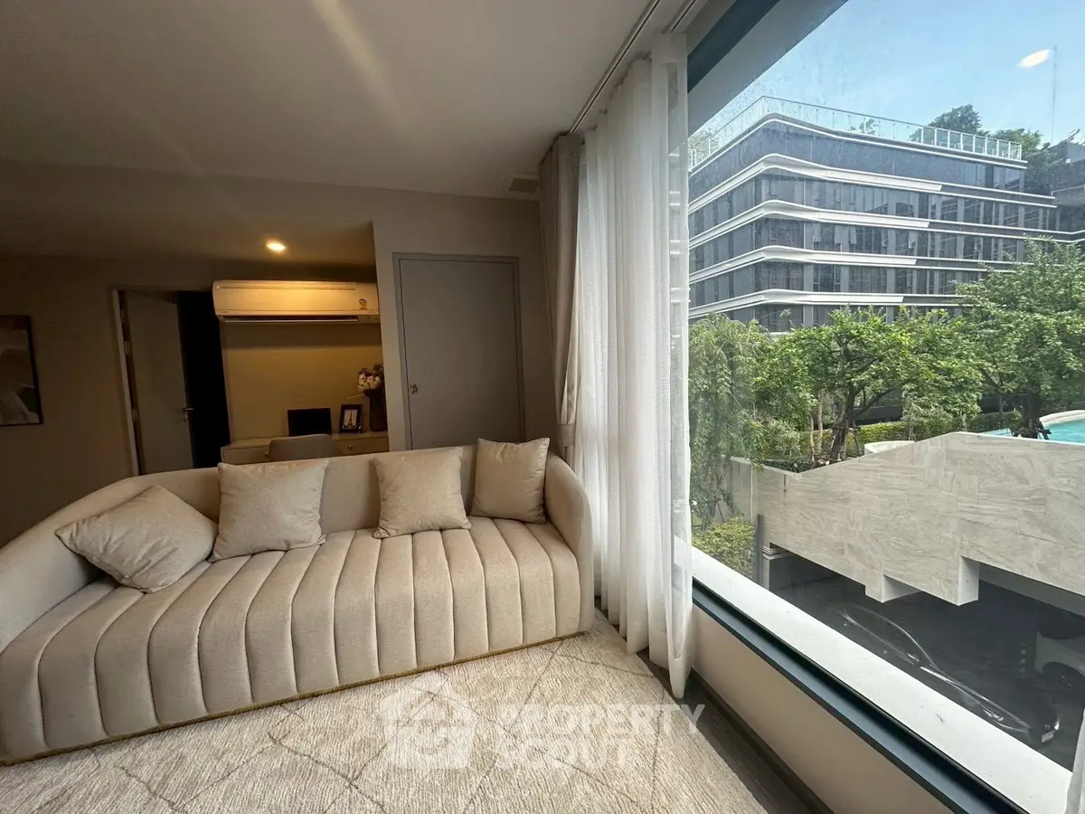 Luxurious living room with modern sofa and large window offering stunning view of contemporary building and greenery.