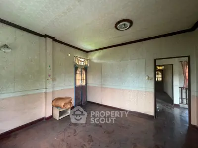 Spacious room with vintage wallpaper and wooden flooring, featuring a small shelf and natural light from windows.