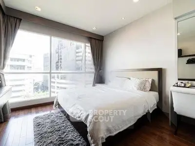 Bright and spacious bedroom with large window and modern decor in urban apartment.