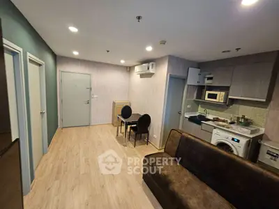 Modern living room with integrated kitchen and dining area, featuring sleek appliances and cozy seating.