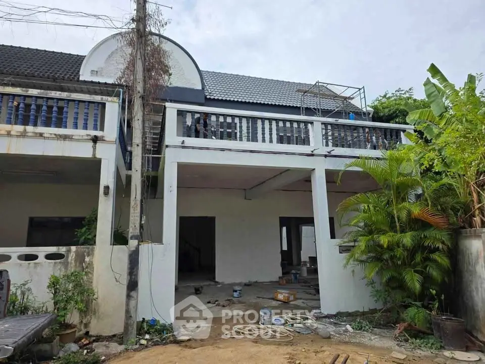 Charming two-story house under renovation with lush greenery and spacious balcony.