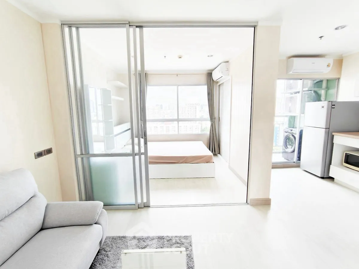Modern open-plan apartment with sliding glass doors and city view, featuring a cozy living area and sleek kitchen.