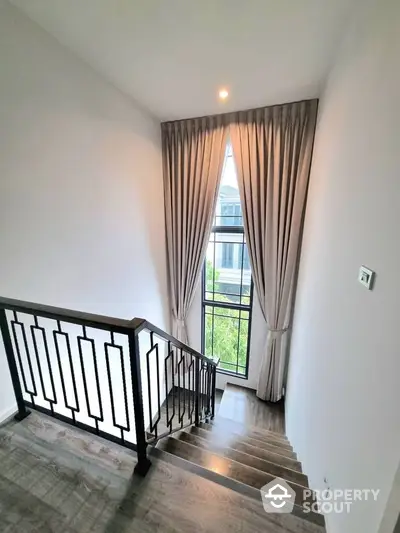 Elegant staircase with modern railing and large window with curtains in a stylish home