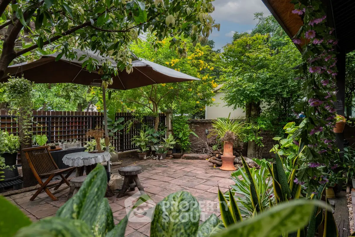Charming garden patio with lush greenery and cozy seating area under an umbrella.