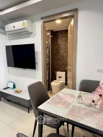 Modern dining area with view into compact bathroom, featuring sleek furniture and wall-mounted TV.