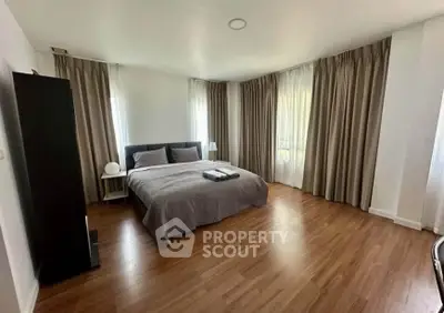 Spacious bedroom with elegant curtains and wooden flooring in modern apartment.