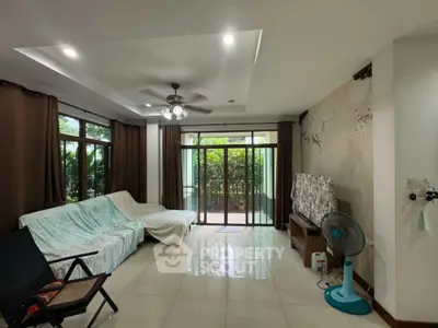 Spacious living room with large windows and garden view, featuring modern ceiling fan and cozy seating area.