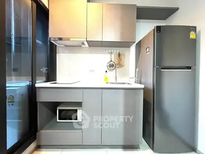Modern compact kitchen with sleek cabinetry, microwave, and refrigerator in a stylish apartment.