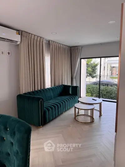 Elegant living room with green velvet sofa and modern coffee table, featuring large windows and stylish curtains.