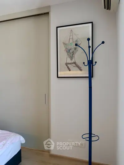 Modern bedroom corner with stylish coat rack and framed artwork, featuring sleek sliding door.