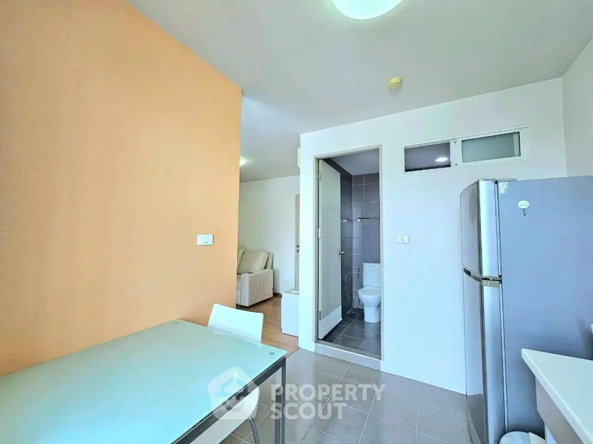 Modern apartment interior with dining area, fridge, and bathroom view.
