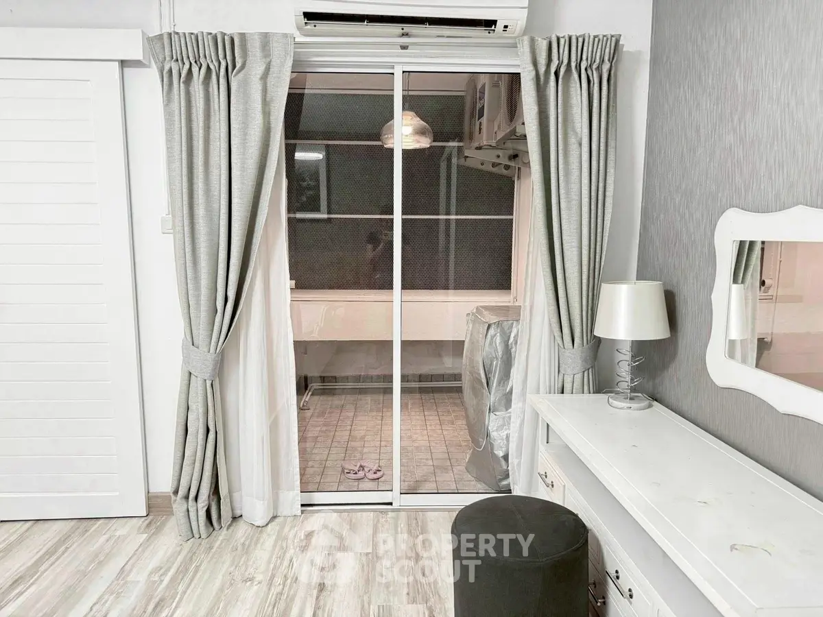 Chic bedroom with sliding glass doors leading to a cozy balcony, featuring elegant curtains and modern decor.
