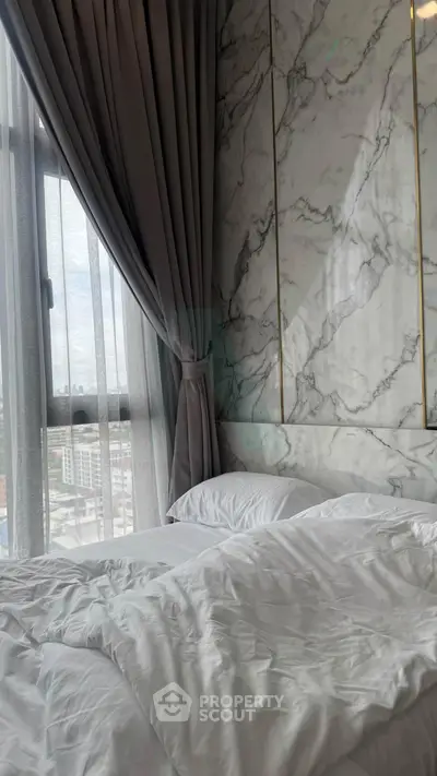 Luxurious bedroom with marble accent wall and city view through large window.