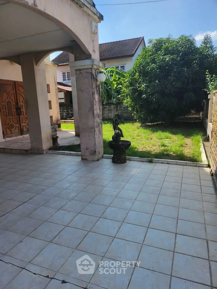 Charming residential entrance with spacious tiled patio and lush garden view.