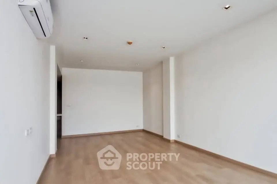 Spacious empty room with wooden flooring and air conditioning unit