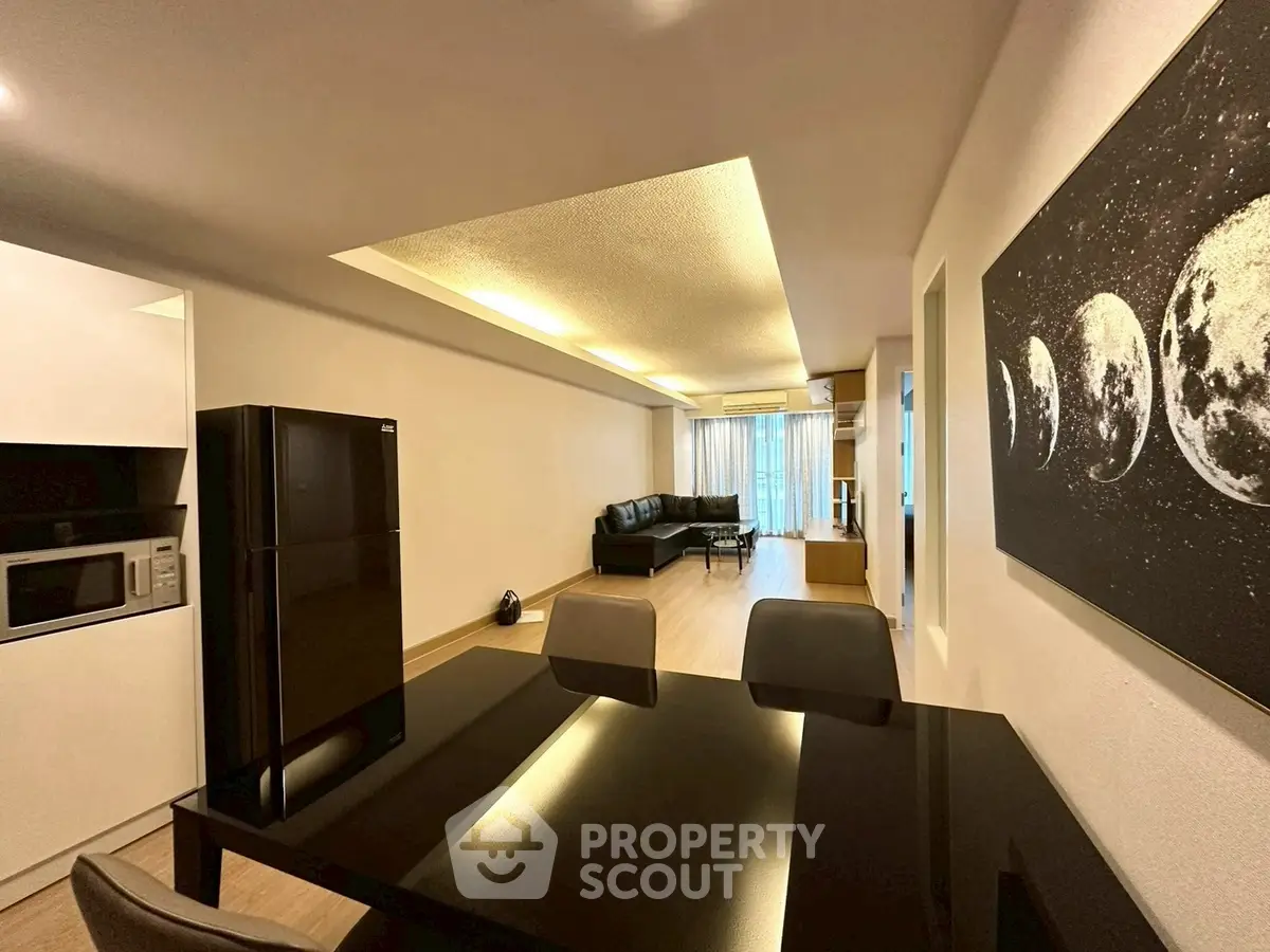 Modern living room with sleek black furniture and moon phase artwork, featuring open layout and natural light.