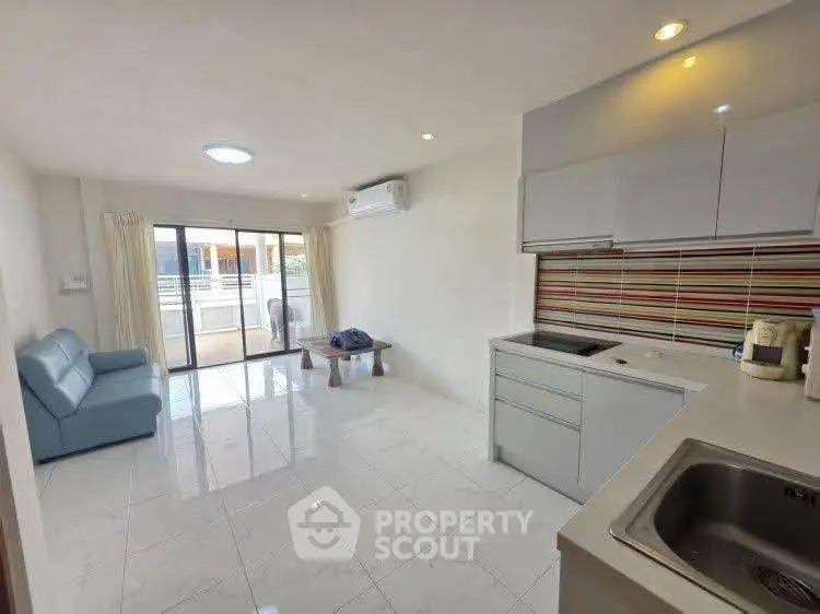 Modern open-plan living room with kitchen, featuring sleek design and balcony access.