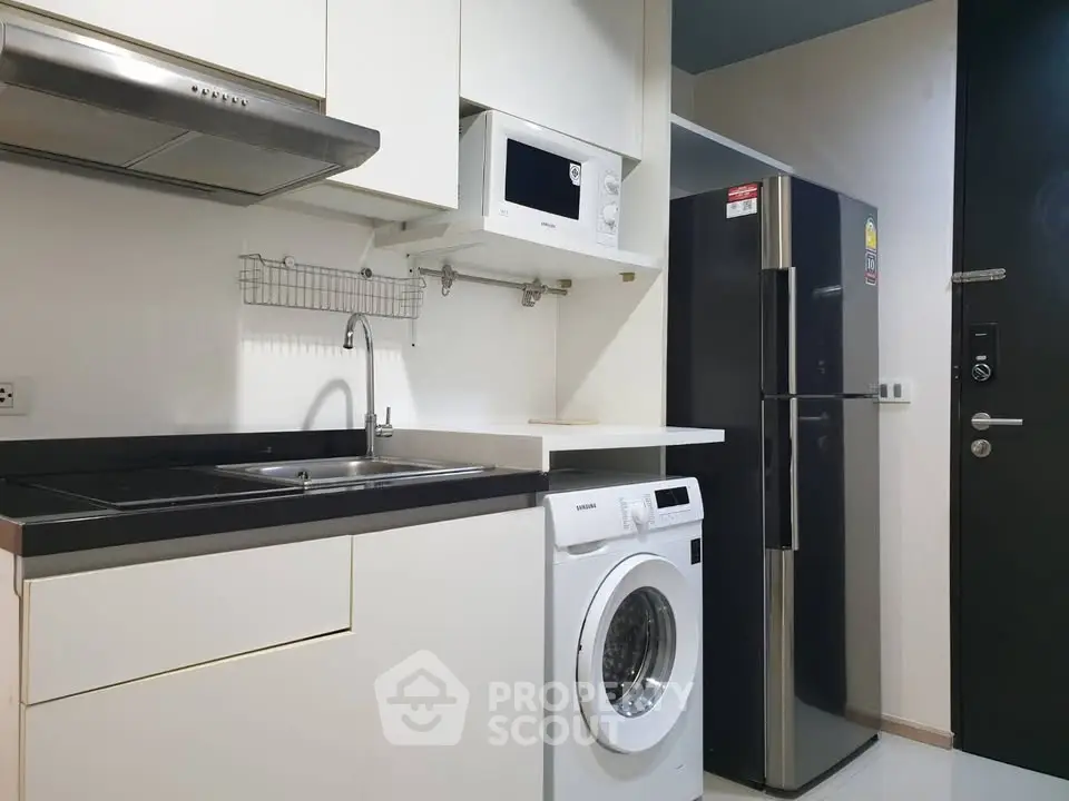 Modern kitchen with sleek appliances including fridge, microwave, and washing machine in compact layout.