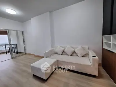 Modern living room with elegant white sofa and ottoman, featuring sleek wooden flooring and ample natural light.