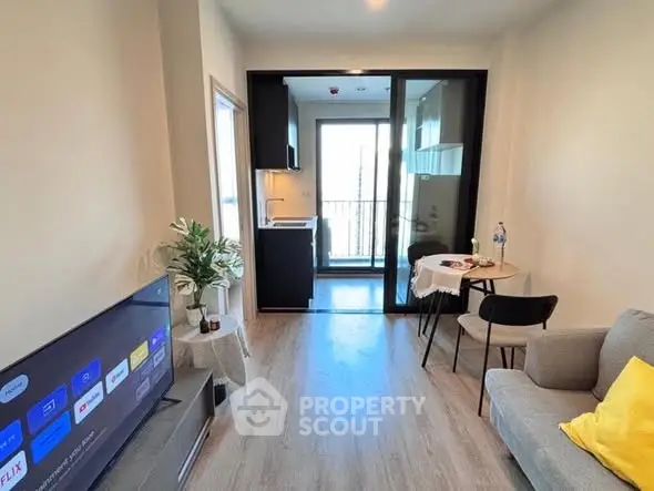 Modern living room with open kitchen and balcony, featuring sleek furniture and natural light.