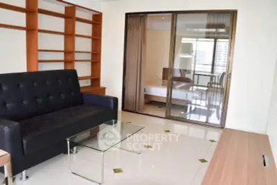 Modern living room with sleek black sofa, glass coffee table, and built-in wooden shelves.