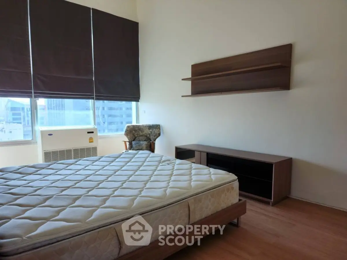Spacious bedroom with large window and modern furniture in a high-rise apartment.