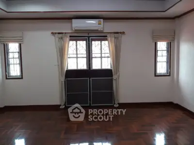 Spacious room with polished wooden floors and large windows, featuring air conditioning for comfort.